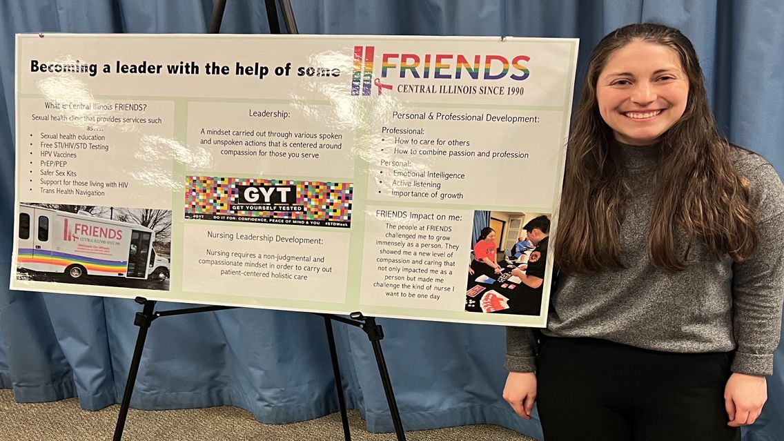 Female student stands by poster of project