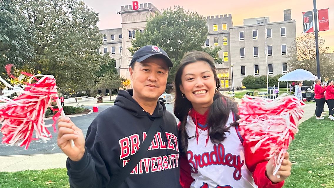 Saim and Adalia Yeung pose in front of Bradley Hall with red and white pompoms.